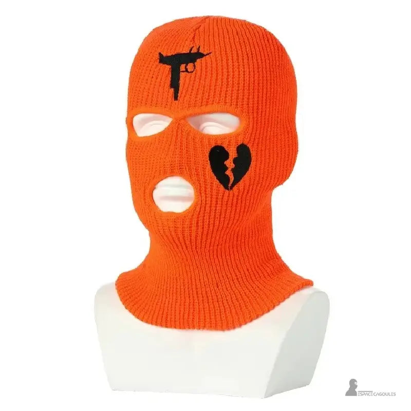 Passamontagna arancione brillante in maglia da gangster con pistola nera e ricamo a cuore spezzato, adagiata su un busto bianco in studio