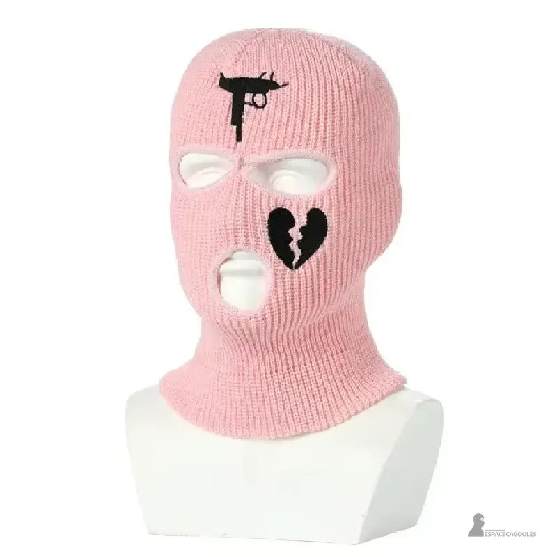 Cagoule gangster rose clair en laine tricotée avec motifs noirs pistolet et cœur brisé, présentée sur mannequin blanc