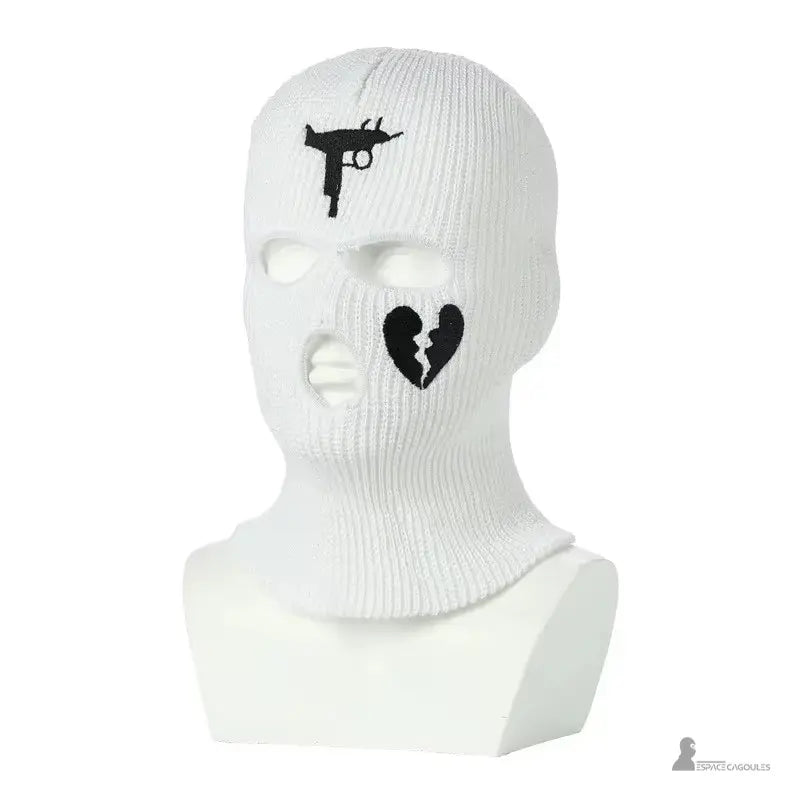 Passamontagna da gangster bianco in maglia, con pistola nera e motivi di cuore spezzato, posata su manichino bianco in studio