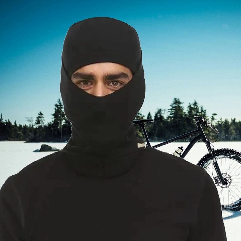 Cyclist wearing a black merino wool balaclava in a winter landscape with snow-covered trees, perfect for cyclists looking for comfort and protection.