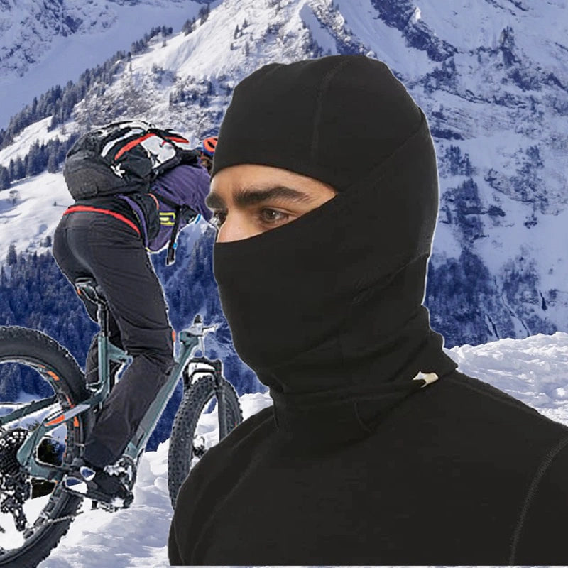 Cyclist wearing a black merino wool balaclava in a snowy mountainous environment, ideal for winter and cold weather bike rides.