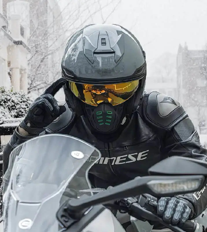 Cyklist utrustad med anti-dimma vintermotorcykel balaclava, svart hjÀlm och gultonade glasögon, i skyddsklÀder pÄ en motorcykel i en snöig miljö, som erbjuder stil och komfort pÄ vintern.