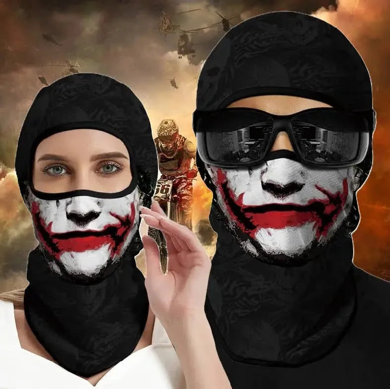 Femme et homme à lunettes de soleil portant la cagoule moto Joker à imprimé visage blanc et sourire rouge, devant un décor de motocross enflammé - Espace Cagoules