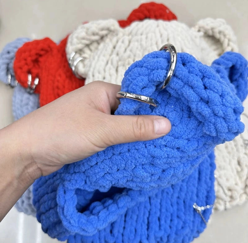 Kapuzenohren aus hellblauem Strick, gefaltet mit strukturierten Details, mit Details der Ringe an den Ohren, neben anderen Modellen in Rot und Beige platziert.