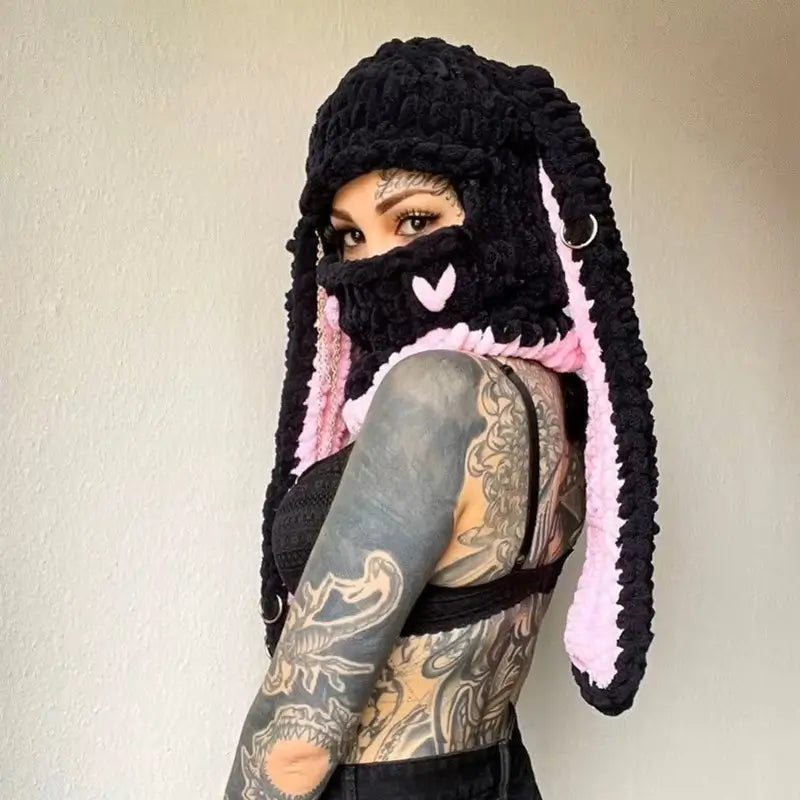 Black and pink rabbit ears balaclava on tattooed mannequin â A tattooed woman wears a black balaclava with long rabbit ears lined with light pink. A bold and cozy look, perfect for a winter streetwear style.