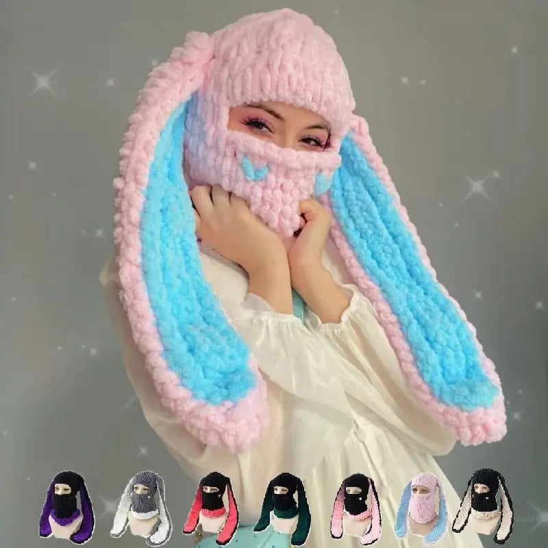 Balaclava Pink and Blue Knit Rabbit Ears â A woman wears a pink soft mesh balaclava with long blue faux fur bunny ears. She poses with a snowy background, perfect for winter.