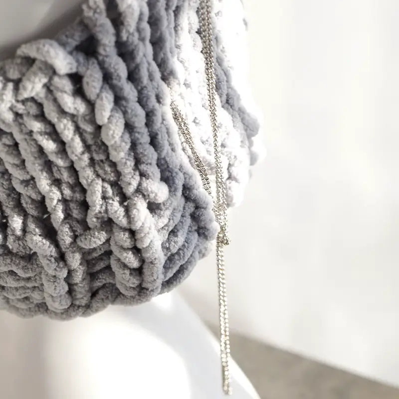 Nahaufnahme einer grauen Strickkapuze mit Ohren, die die Details der dicken Strickwaren und der dekorativen Kette hervorhebt.
