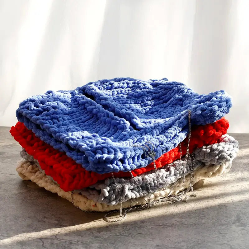 Ein Haufen Sturmhaubenohren, erhältlich in Blau, Rot und Grau, platziert auf einer Betonfläche, die von natürlichem Licht beleuchtet wird.