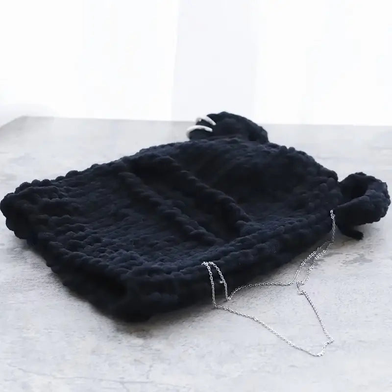 Kapuzenohren aus schwarzer Strickwolle, sorgfältig flach auf eine sonnige Oberfläche gelegt, ideal für den Winter.