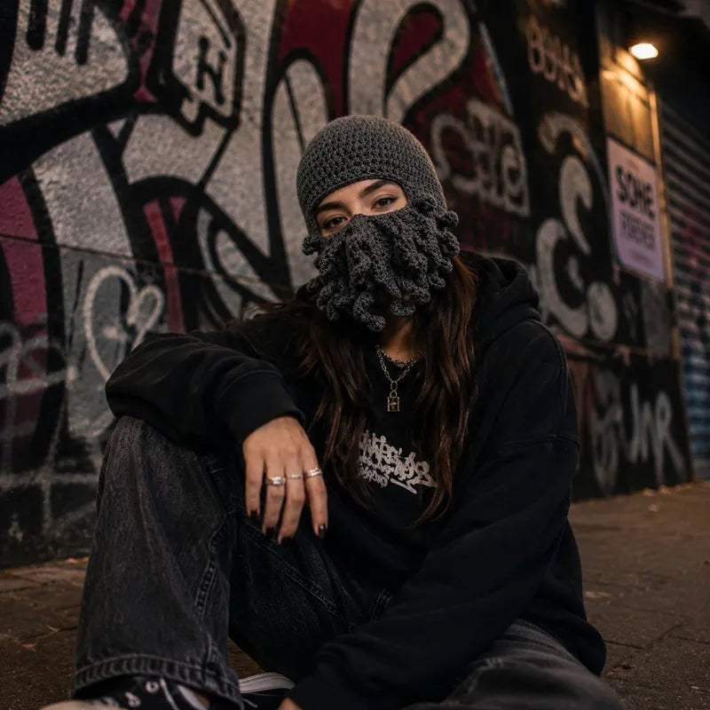 Femme en tenue streetwear portant une cagoule pieuvre grise devant un mur de graffitis - Espace Cagoules
