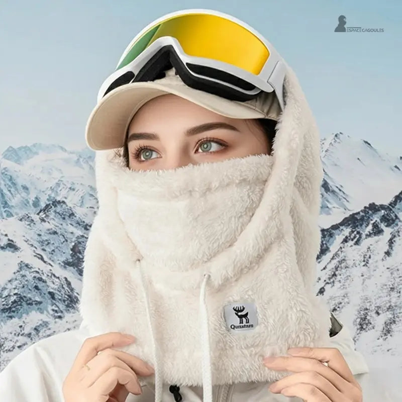 Cagoule polaire Femme blanche portée par une femme en extérieur avec casquette et masque de ski, fond de montagnes enneigées