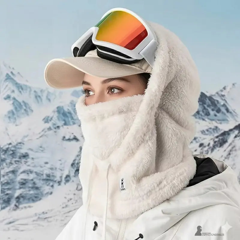 Cagoule polaire Femme blanche portée avec casquette et lunettes de ski colorées, mise en avant en extérieur sur fond alpin