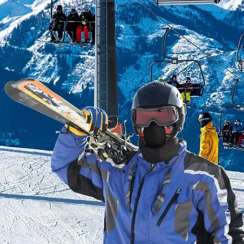 Skier holding his snowboard in resort, wearing a red ski helmet balaclava, surrounded by a snowy mountain landscape.