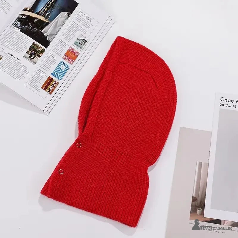 Cagoule Rouge posée à plat sur une surface blanche avec des magazines, montrant les détails de sa texture en tricot côtelé