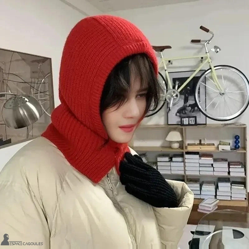 Cagoule Rouge portée par une femme en intérieur, associée à une doudoune beige et des gants noirs, ambiance hivernale chaleureuse