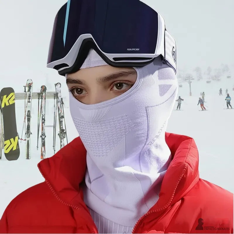 Cagoule ski femme blanche portee avec combinaison rouge et masque de ski sur piste enneigee en arriere plan