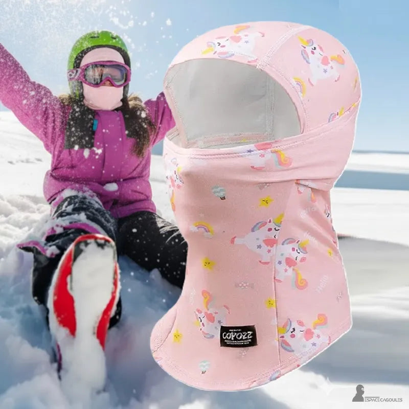 Rosa flicka skidbalaclava med enhörningsmönster, bärs av ett barn som leker i snön, perfekt för vinteraktiviteter – Espace Cagoules