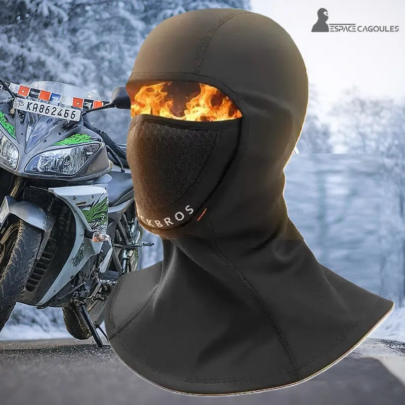 Motorcykel termisk balaclava â Helsvart balaclava med en flamma visuell effekt, framför en motorcykel parkerad pĂ„ en snöig vĂ€g, för att illustrera skydd mot extrem kyla pĂ„ vintern.