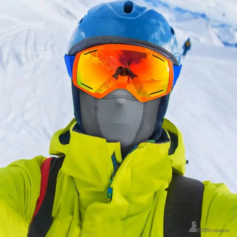 Graue Ski-Nackenkapuze, die von einem Skifahrer mit gelber Jacke und blauem Helm getragen wird, ideal für Wintersport und hohe Berge