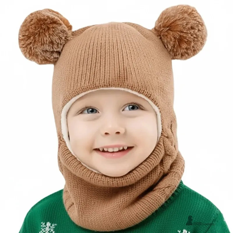 Cagoule tricot enfant marron clair avec pompons ronds, petit garçon souriant en intérieur portant un pull vert de Noël