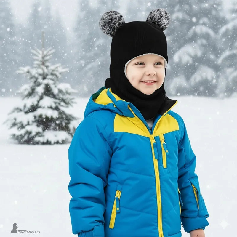 Cagoule tricot enfant noire avec pompons gris, petit garçon souriant en manteau bleu dans un paysage enneigé