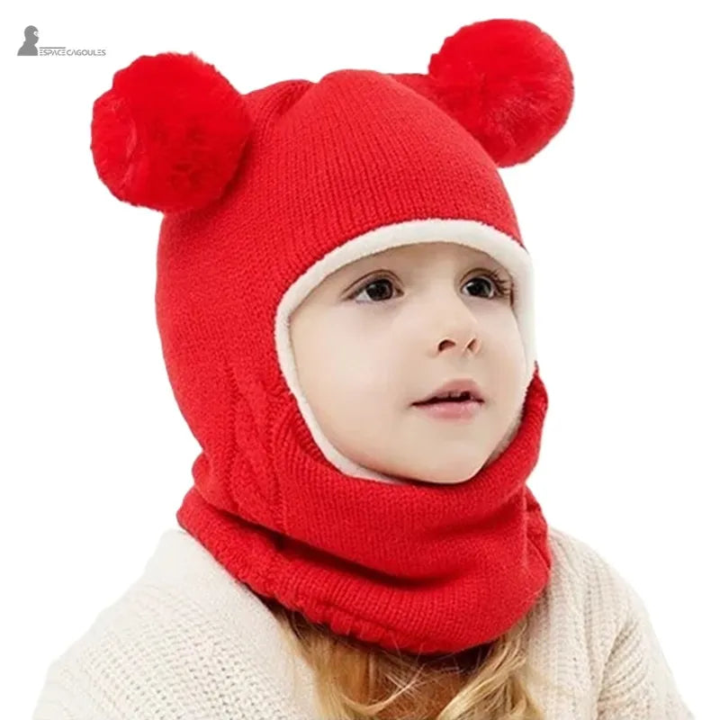 Cagoule tricot enfant rouge avec pompons ronds, fillette vue de face en intérieur avec cagoule baissée et contour blanc
