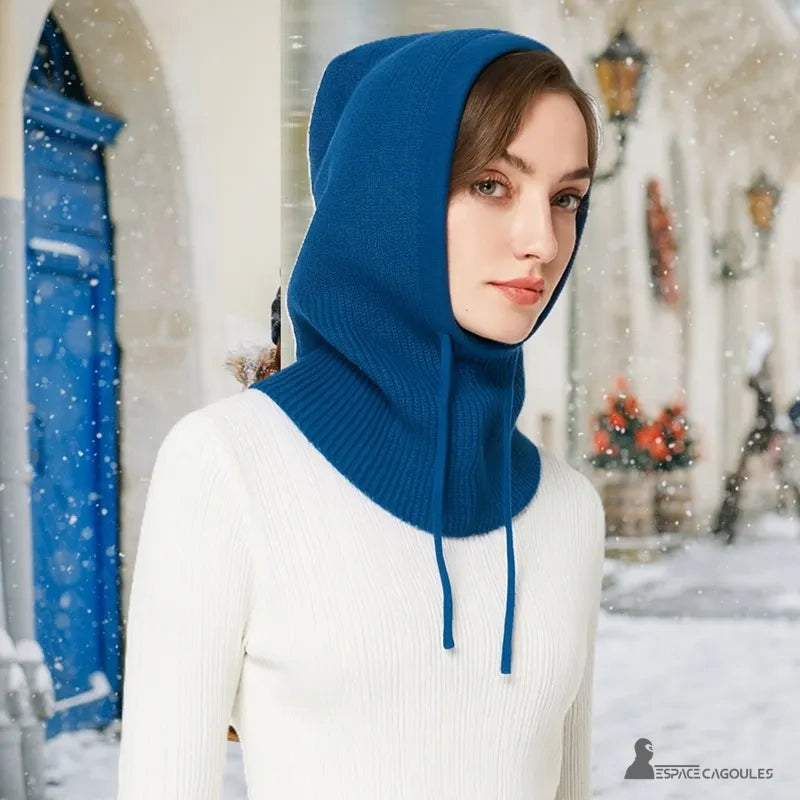 Bright blue woman knitted balaclava worn by model outdoors under snow, elegant urban background with blue door in background