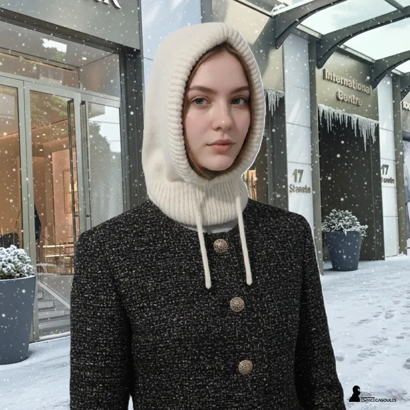 Strickmütze für Frauen in Beige, getragen mit einem schicken Mantel in einer urbanen Winterlandschaft, elegante Kapuze, die Schutz für Hals und Kopf bietet – Cagoules Raum