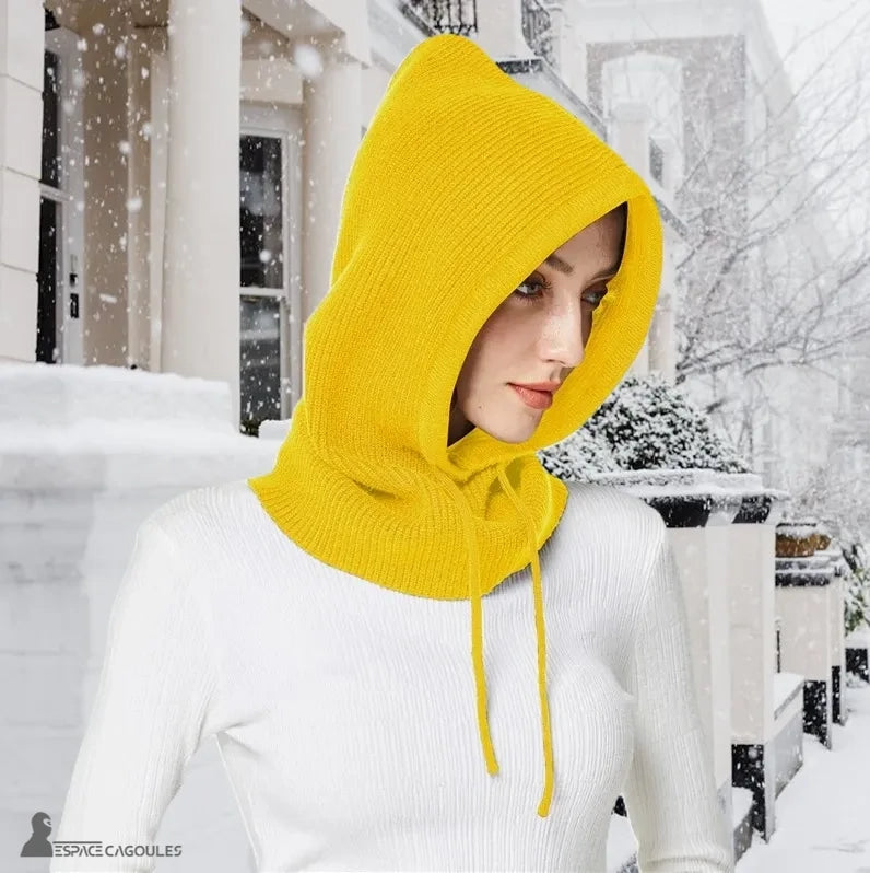 Bright yellow women's knitted balaclava worn by model outdoors in the snow in front of elegant building