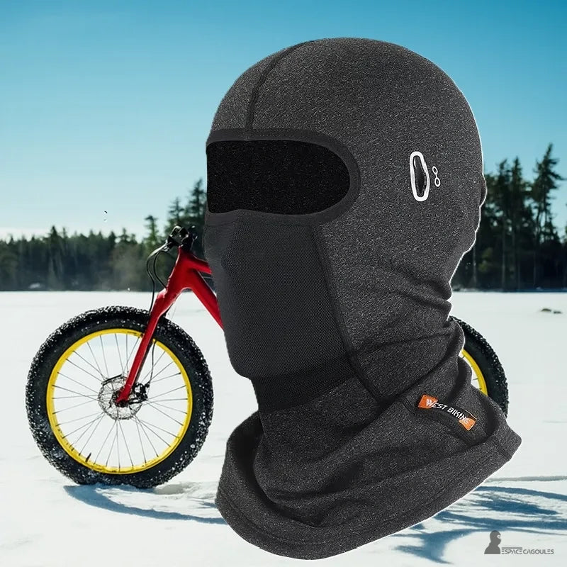 Cagoule vélo hiver grise portée devant un vélo rouge sur neige, adaptée aux environnements froids