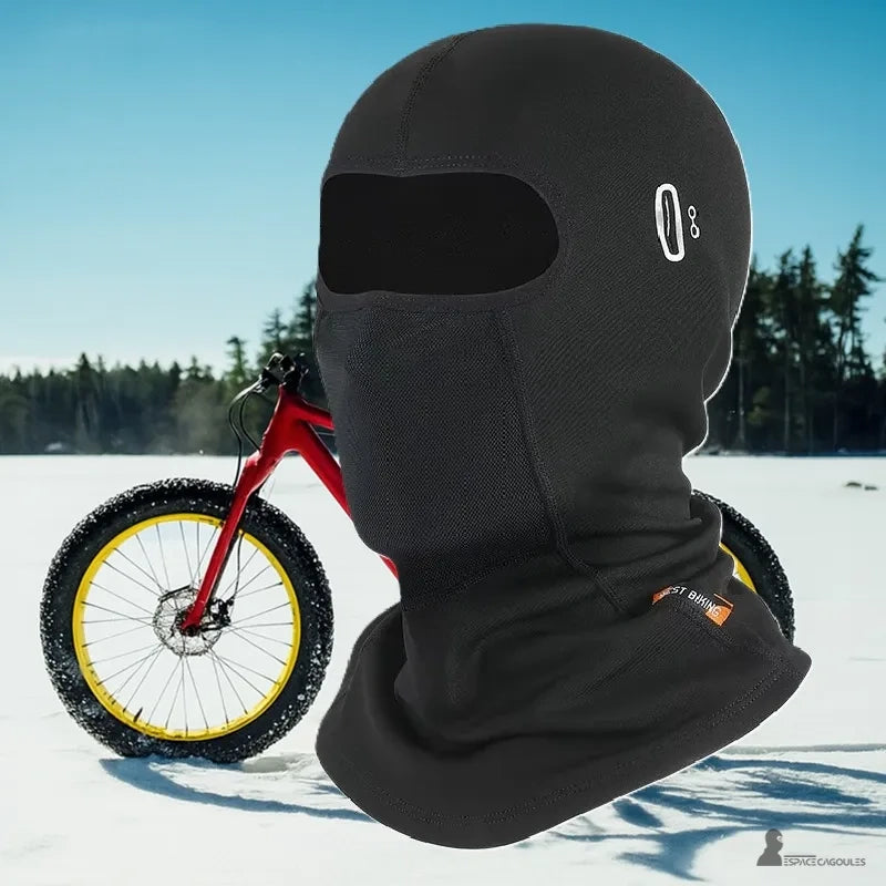 Cagoule vélo hiver noire portée en extérieur sur fond enneigé avec un vélo rouge et jaune