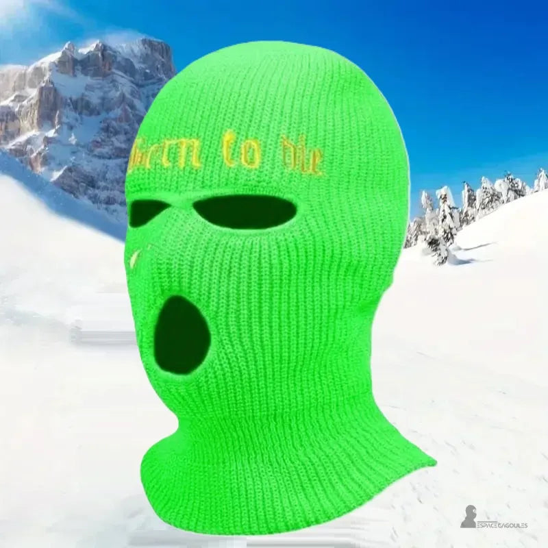 Bestickte fluoreszierende grüne Sturmhaube, präsentiert in einem verschneiten Berg unter blauem Himmel, warme und sichtbare Wintersportausrüstung