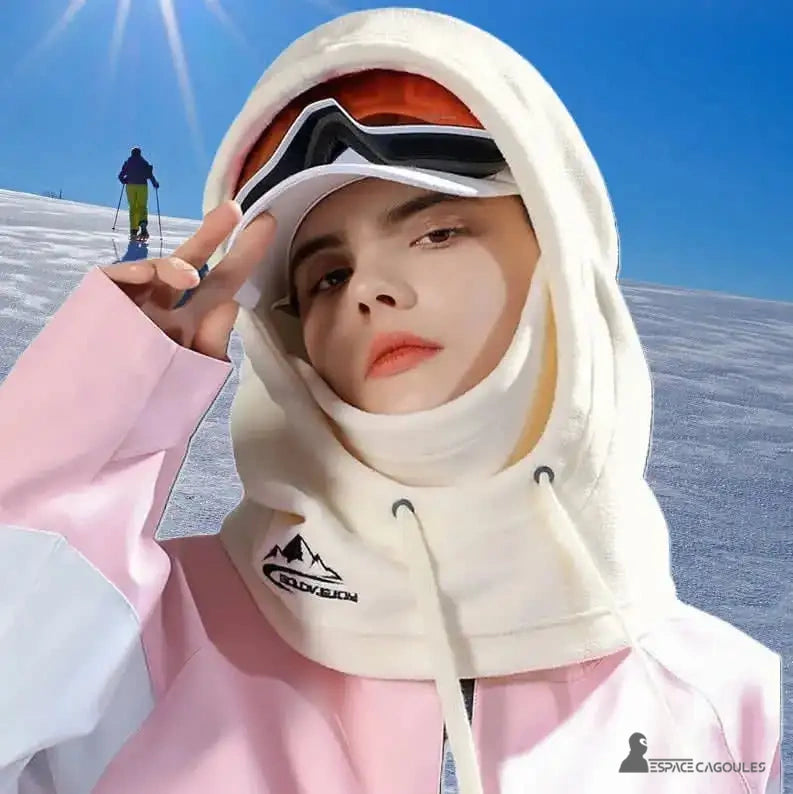 Beige women's balaclava hood, worn outdoors on a snowy ski slope, with a mountain logo. One person wears ski goggles and a pink and white jacket.