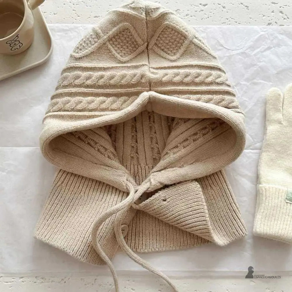 Cappuno Passamontagna beige a maglia posata su un tavolo, dettagli a treccia e bottoni, protezione morbida dal freddo