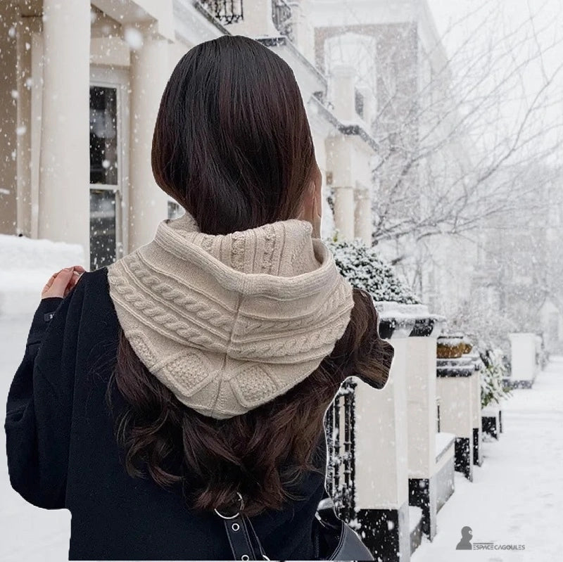 Passamontagna beige in maglia con cappuccio vista da retro, donna che cammina nella neve con un cappotto nero, comfort ed eleganza per l'inverno