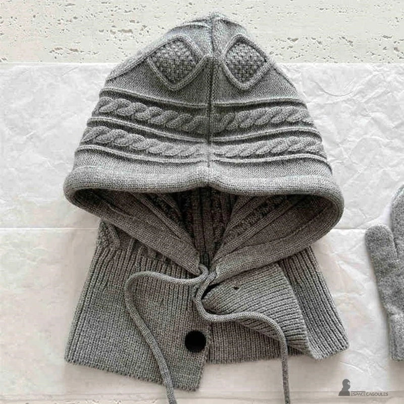 Cofano Passamontagna a maglia grigio posata su un tavolo, spessa maglia a trecce e chiusura dei bottoni, calore e praticità