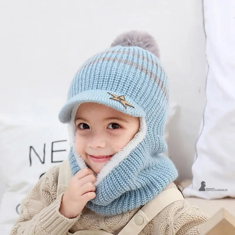 Casquette bonnet enfant bleu clair en tricot chaud avec pompon gris, garçon souriant à l’intérieur sur un canapé