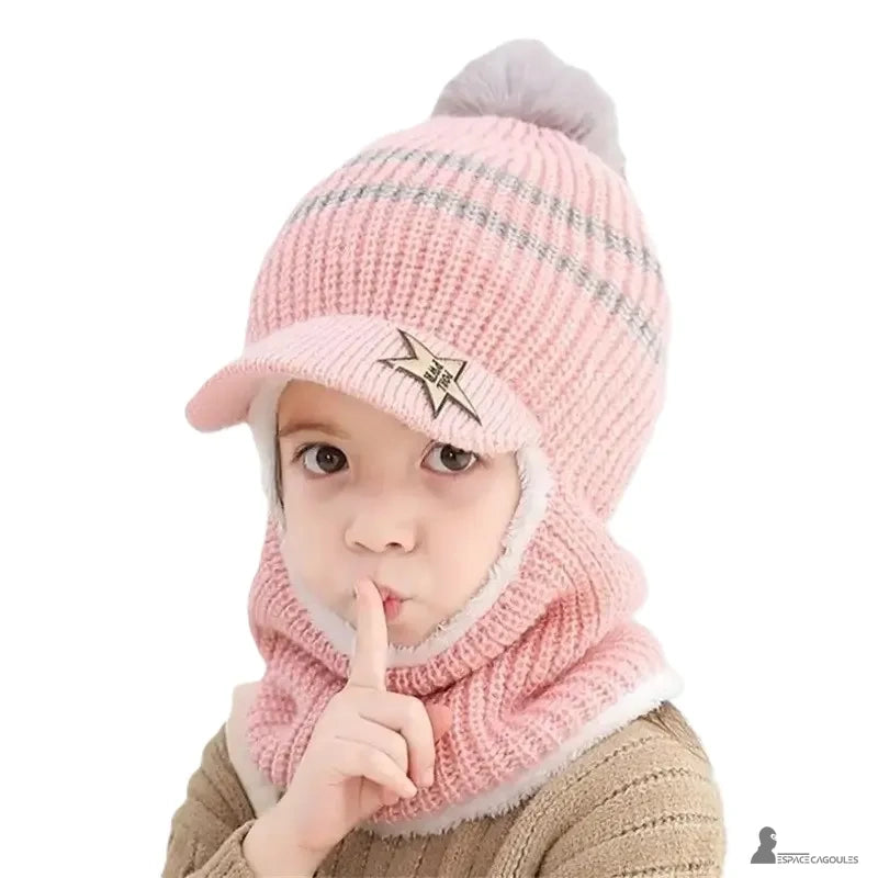 Casquette bonnet enfant rose tricot avec pompon gris et visière, petite fille fait le geste du silence avec son doigt