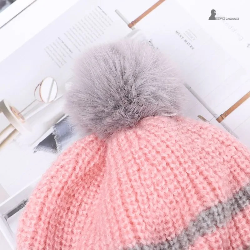 Casquette bonnet enfant rose tricot avec gros pompon gris, gros plan sur le détail du bonnet posé sur une table