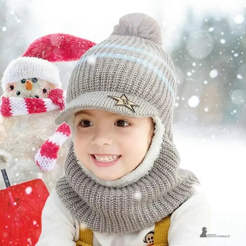 Casquette bonnet enfant gris tricot avec pompon et rayures bleues, garçon souriant dehors dans la neige devant un bonhomme de neige