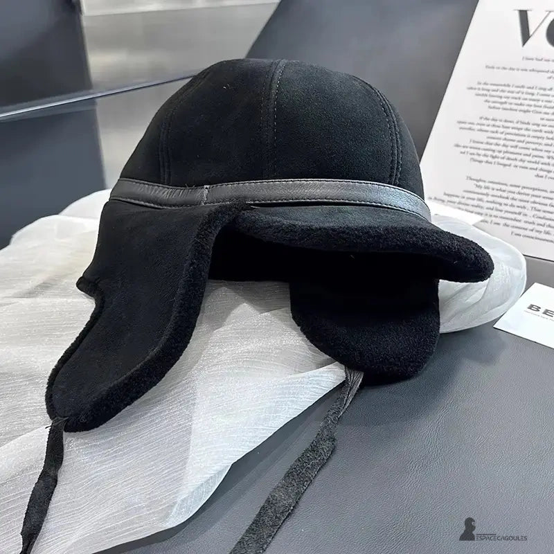 Svart hattkeps med vikta öronlappar placerad på en modern fåtölj