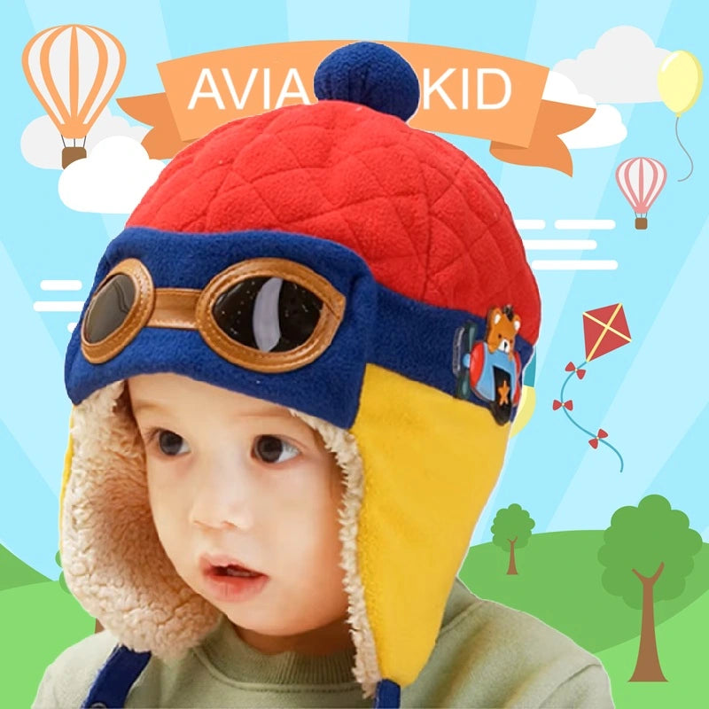 Colorful aviator children's hat, with orange glasses and warm lining, worn by a child in front of an illustration of hot air balloons.