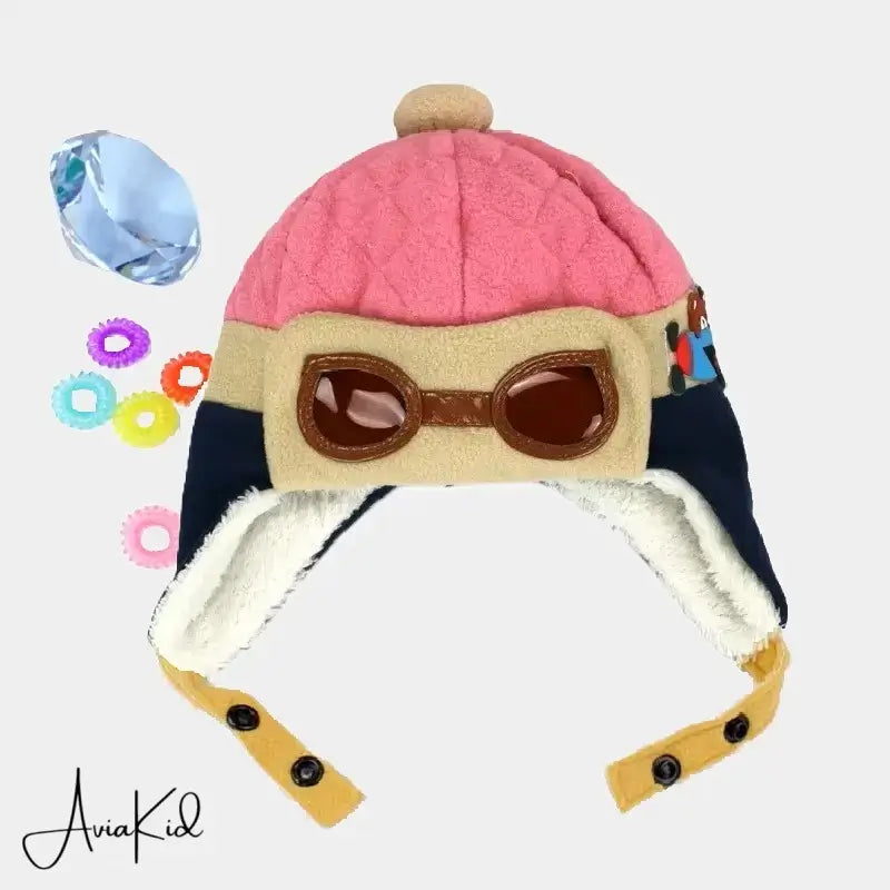 Pink and beige aviator children's hat, with brown aviator glasses and beige pompom, set on a white background with colorful beads.