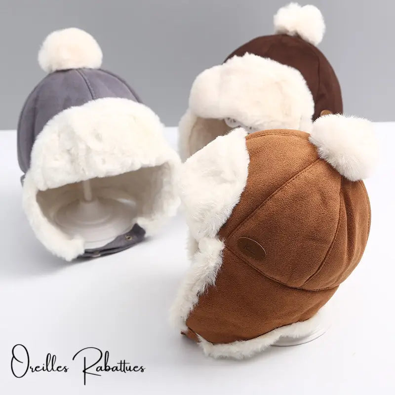 Three children's hats in coffee, brown and grey suede with warm faux fur lining and pompom, photographed against a neutral background. Comfortable and stylish winter protection.
