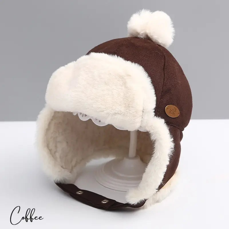 Brown suede children's hat with white faux fur interior, soft pompom and fold-over ear flaps. Perfect for a warm and cozy winter.