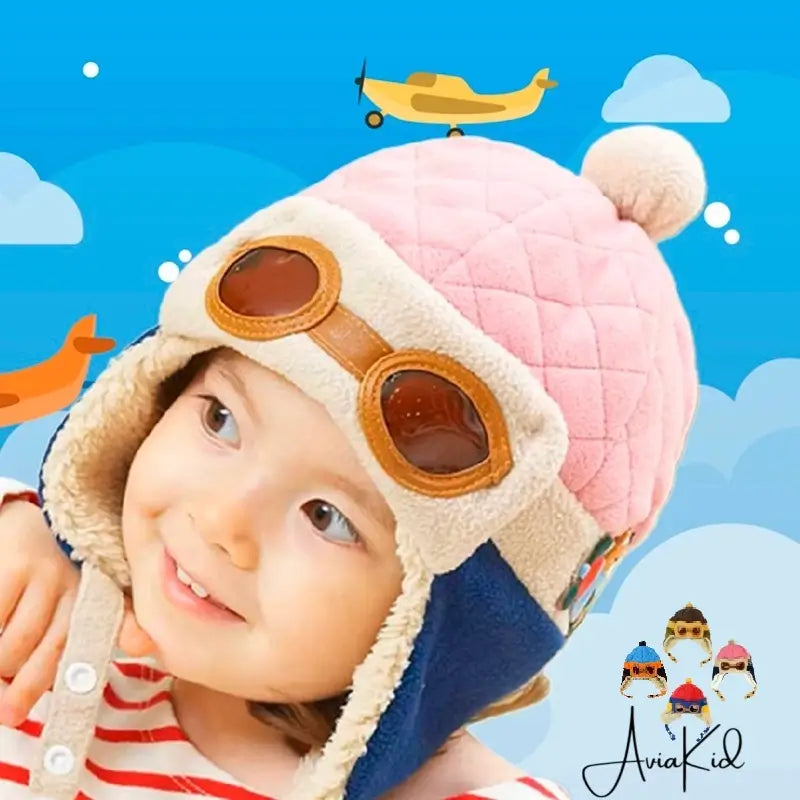 Smiling child with a pink and beige aviator child hat, equipped with glasses, in front of a background illustrated with clouds and an airplane.