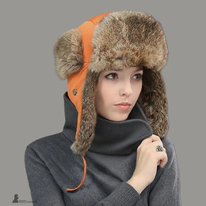 Cappello da donna in pelliccia – Donna con un cappello arancione rifinito con pelliccia vera, giacca grigio scuro, sfondo neutro, atmosfera invernale – Espace Cagoules