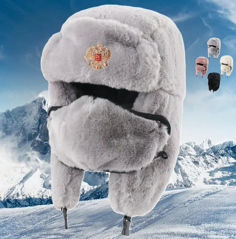 Chapka Russe Impériale en fausse fourrure grise, avec insigne orange sur le front, protège-oreilles rabattables et cache-visage, mise en valeur sur un fond de montagne enneigée. En arrière-plan, plusieurs modèles de chapkas disponibles, offrant chaleur et élégance pour affronter l'hiver.