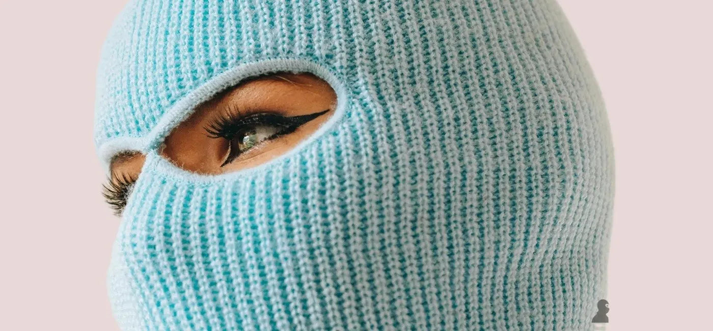 Cagoule 2 trous bleue en maille tricotée portée par une femme au maquillage soigné, mise en avant sur fond rose clair – Cagoule 2 Trous -Espace Cagoules