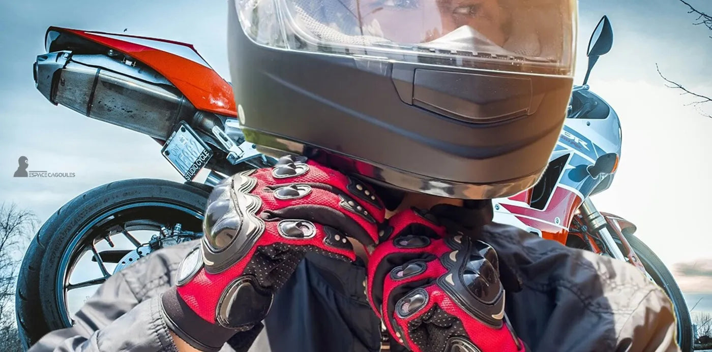 Cagoule moto noire portée sous un casque intégral, motard ajustant la sangle avec des gants rouges devant une moto de sport – Cagoule Moto -Espace Cagoules